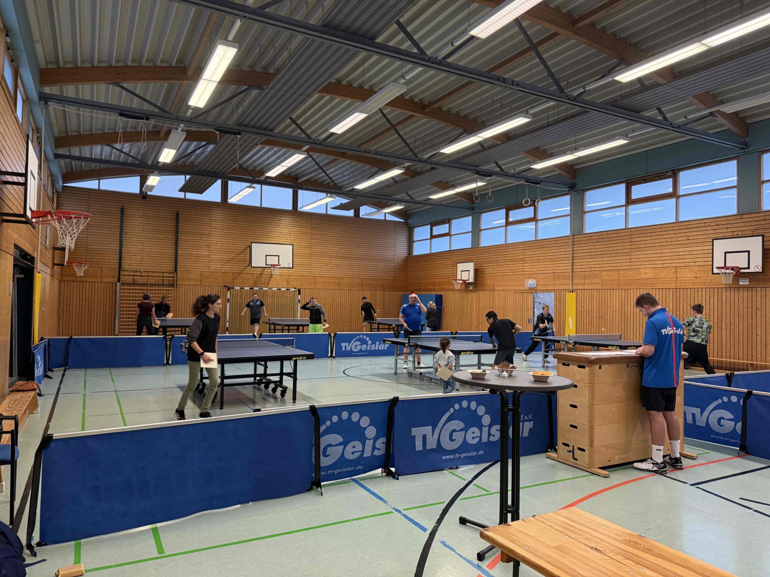 Tischtennishalle mit Platten und spielenden Personen